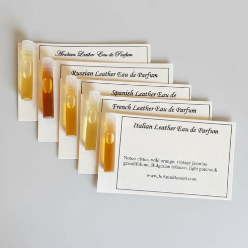 JoAnne Bassett artisan leather perfume sample set five 1ml glass vials fanned out with description cards for Arabian Leather, Russian Leather, Spanish Leather, French Leather, and Italian Leather Eau de Parfum
